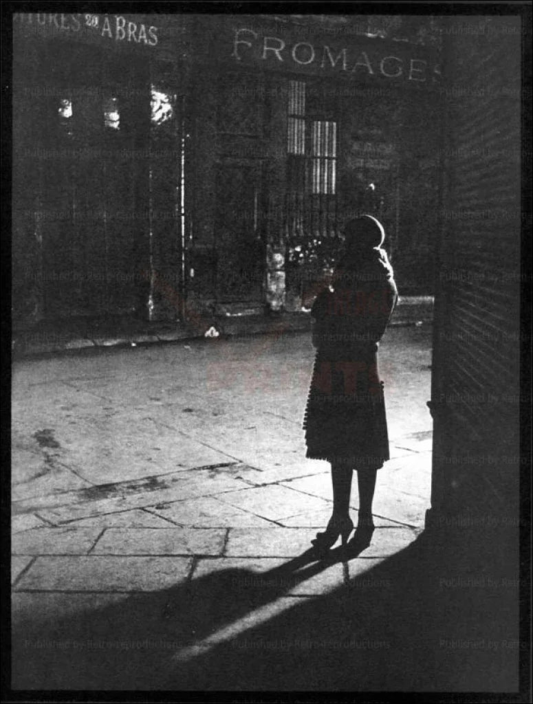 A woman standing in a Paris Street at Night - VINTAGEARTREPRINTS.COM